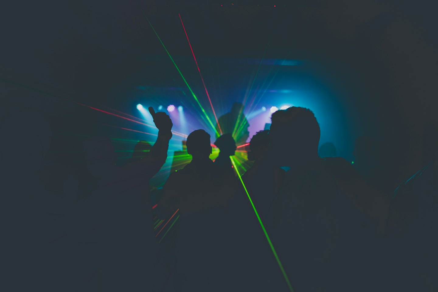 Concert attendees with arms raised watch colorful stage lights.