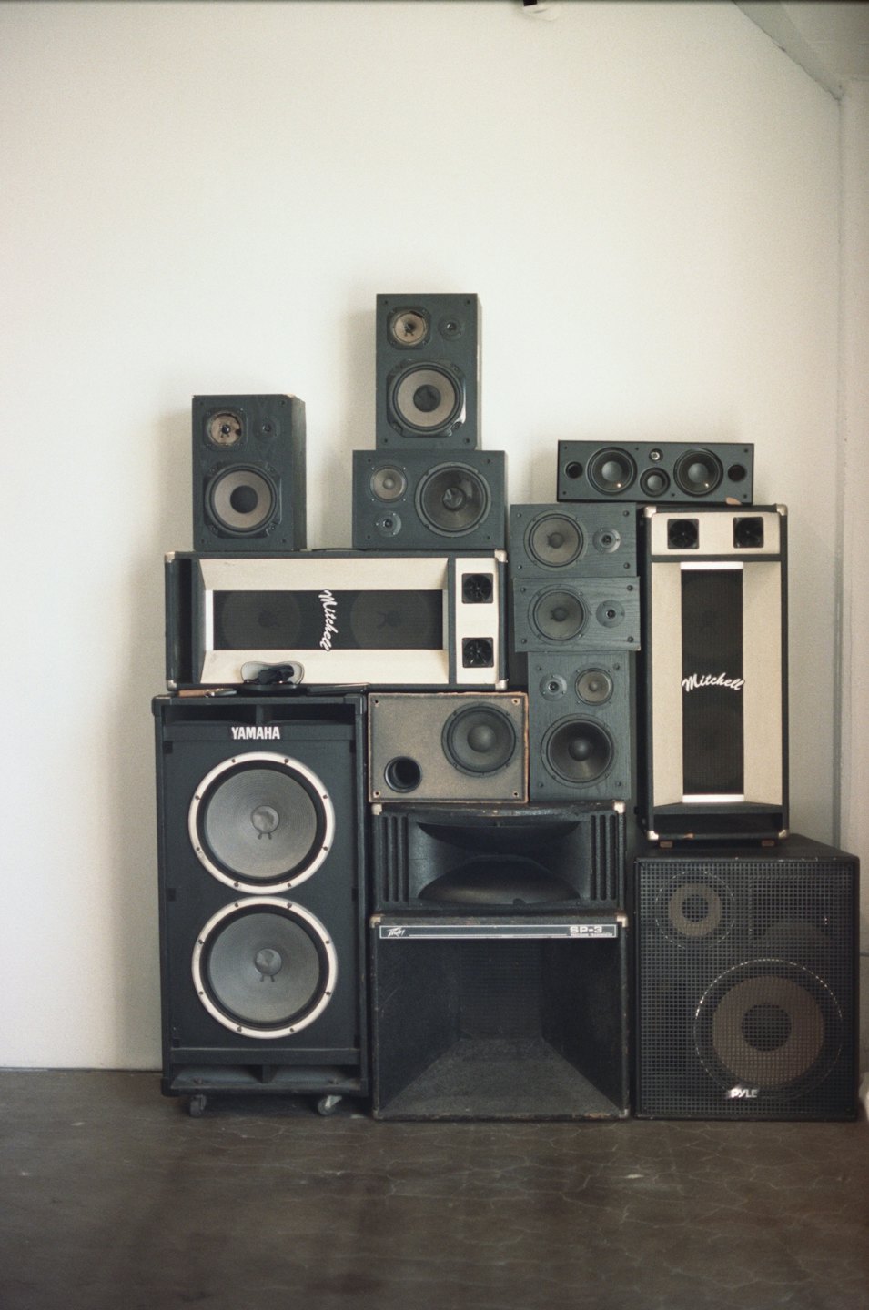 Stacked vintage and modern audio speakers stand against a wall.